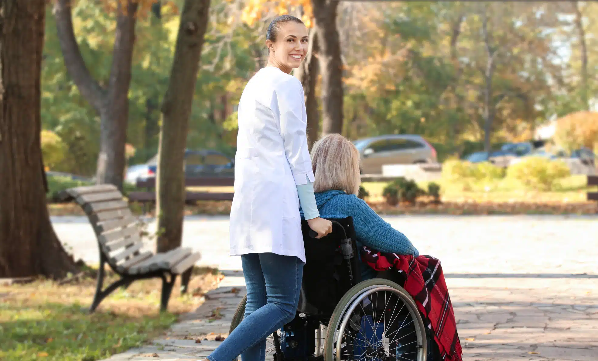 profesional de la asistencia personal empujando a una mujer en silla de ruedas