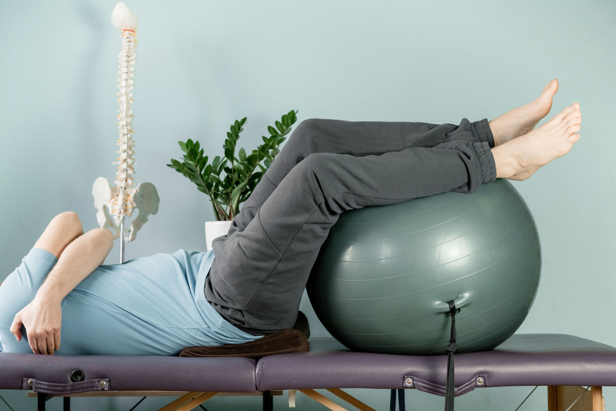 Hombre tumbado con problema en la espalda realiza ejercicios sobre pelota de yoga o pilates